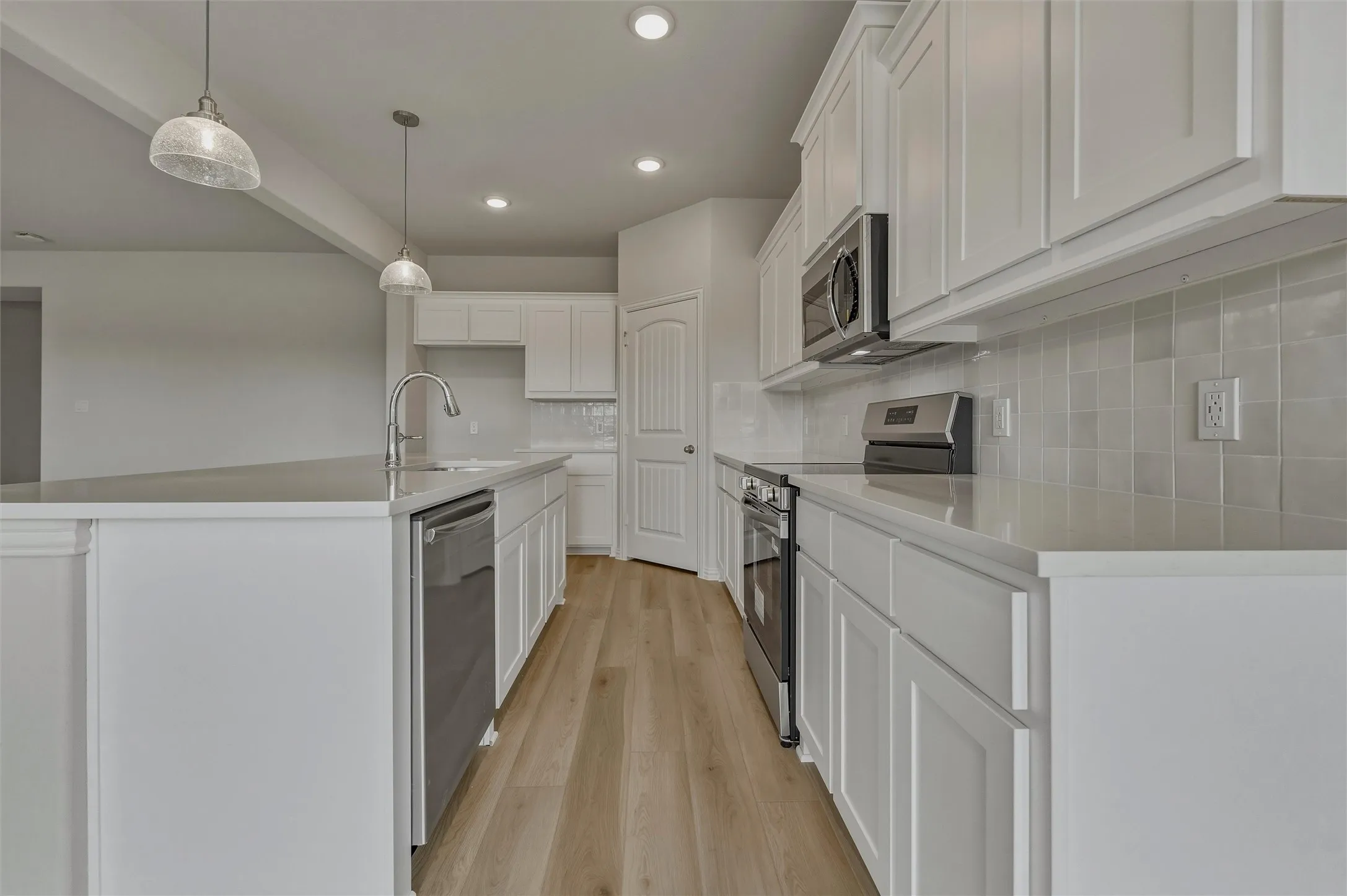 Well-appointed kitchen featuring light wood-finish flooring, white cabinetry, stainless steel appliances, and recessed lighting