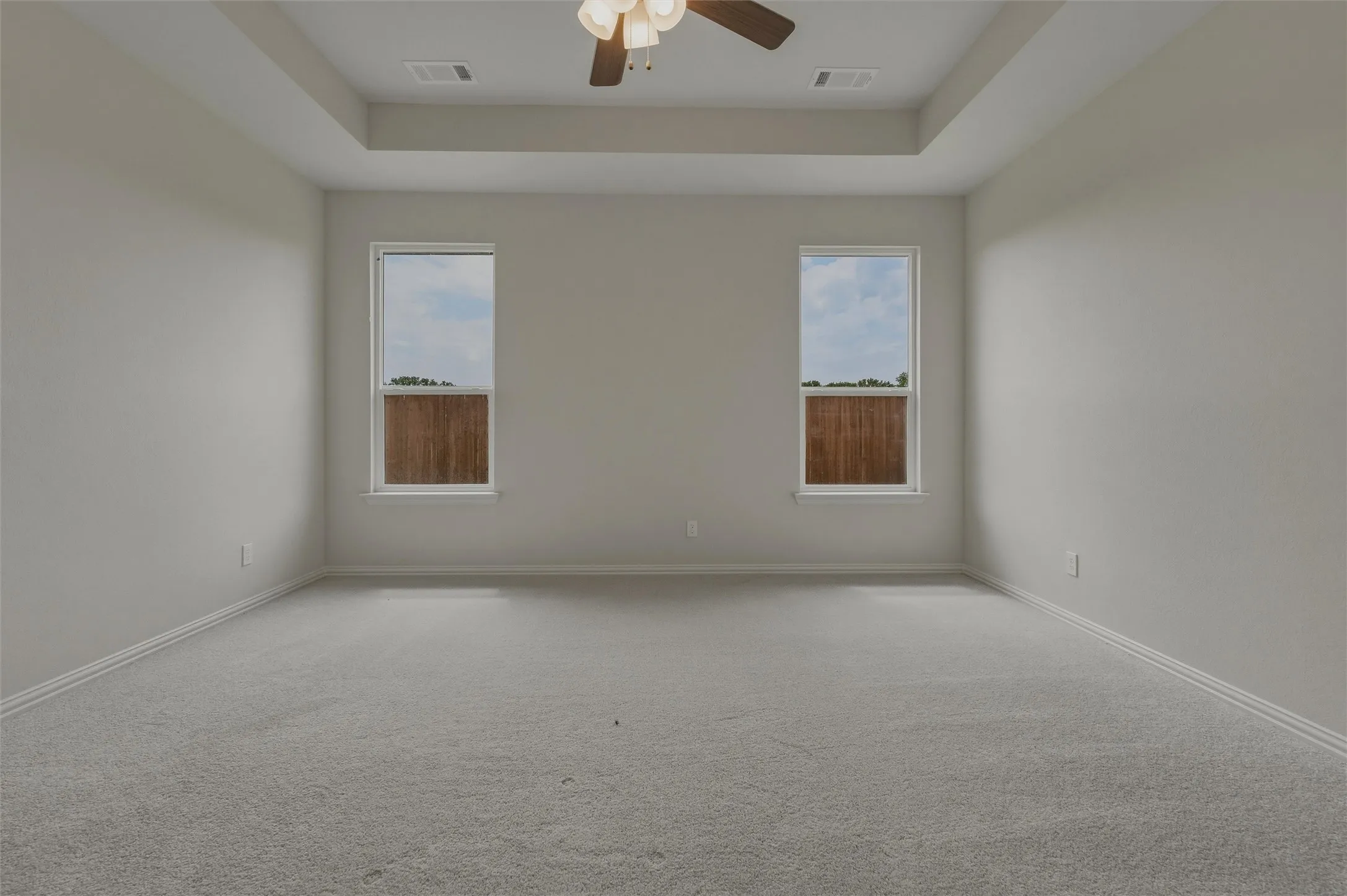 Tray ceiling with integrated ceiling fan, light gray wall paint, and two windows