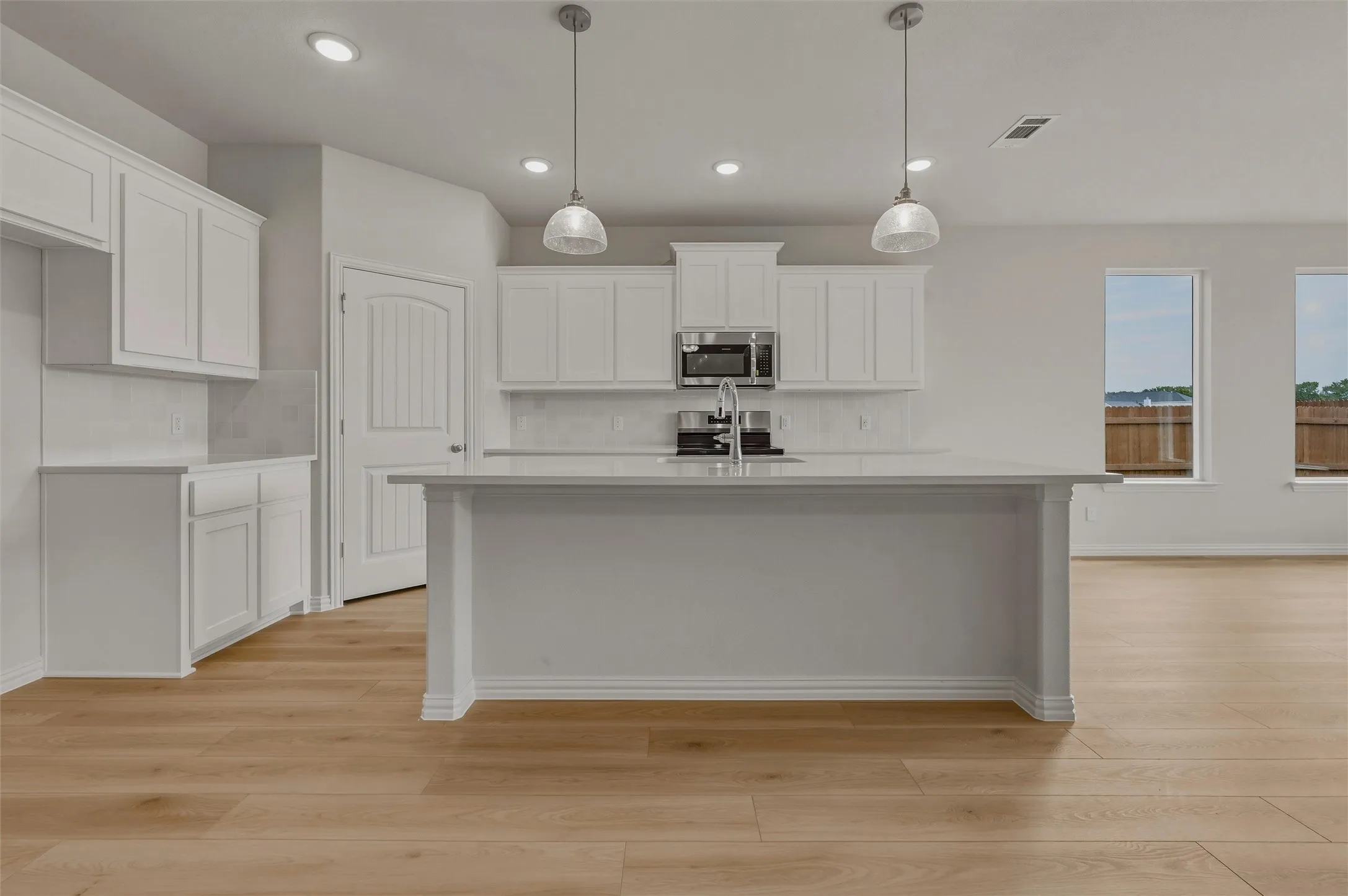 Kitchen featuring an island, white cabinetry, integrated stainless steel microwave, light wood-finish flooring, and pendant lighting