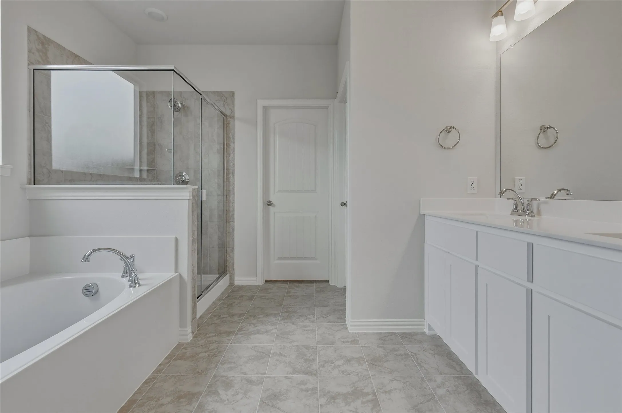 Dual sink vanity with white cabinetry, glass-enclosed shower, built-in soaking tub, and tile flooring