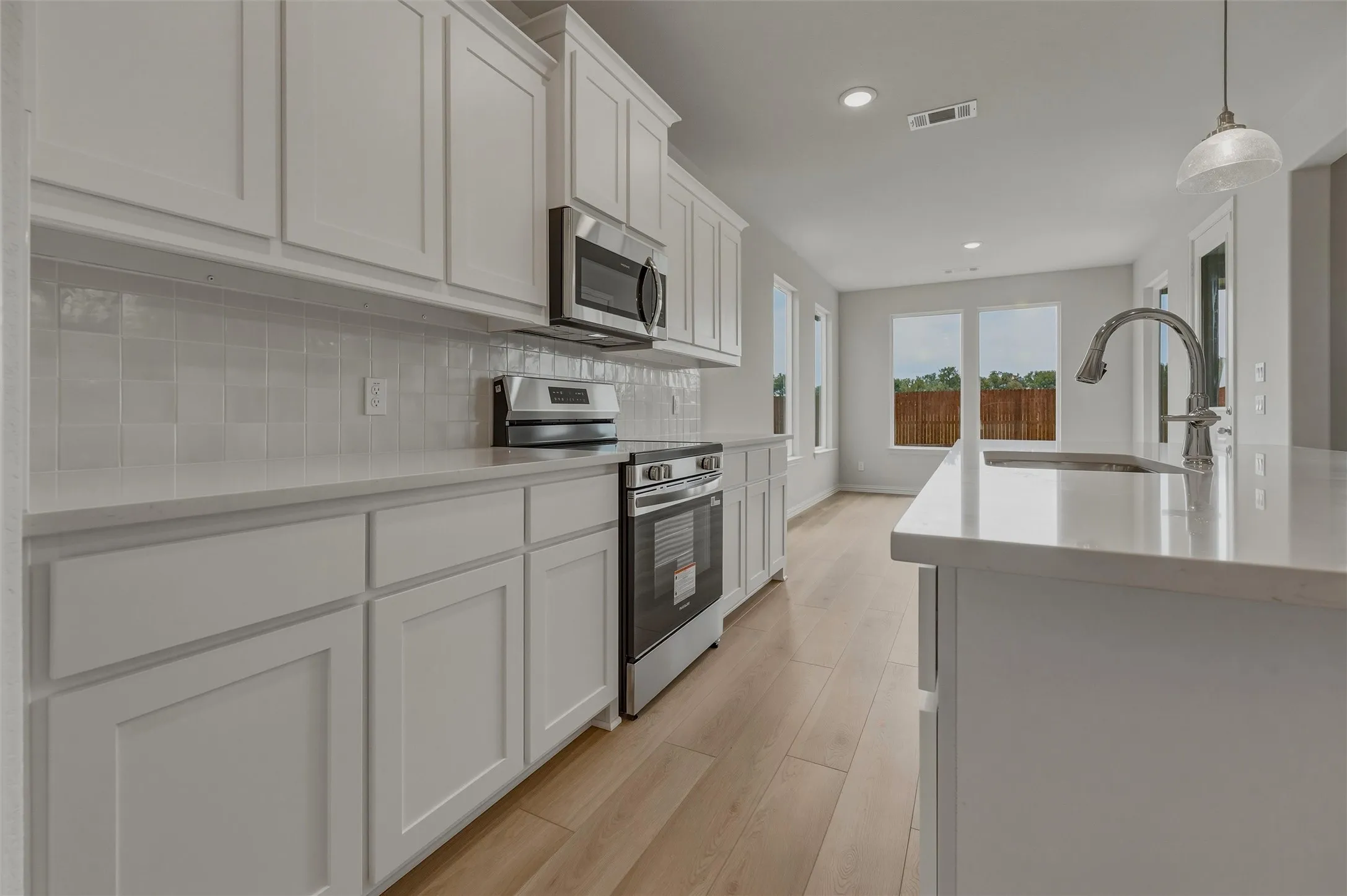 White shaker-style cabinetry, stainless steel appliances, light-toned wood-finish flooring, white countertops, and a white tiled backsplash