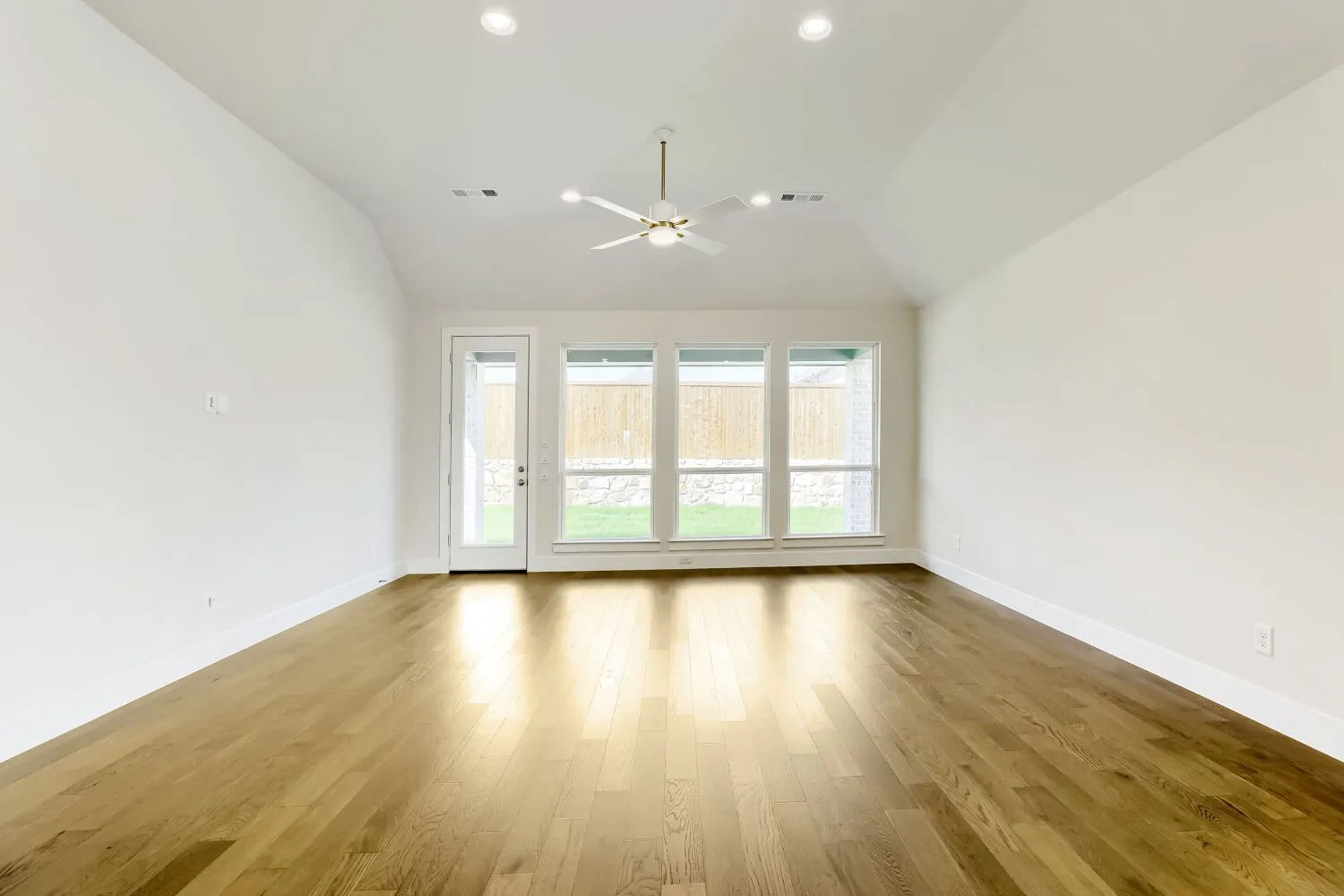 Wood-finish flooring, vaulted ceiling, recessed lighting, ceiling fan, and large windows with a transom door