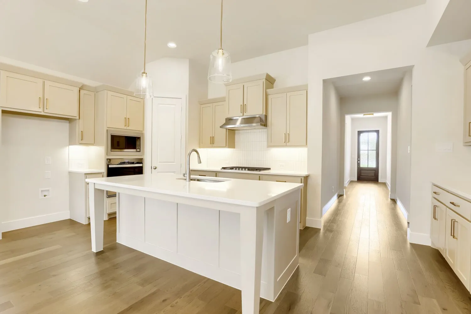 Kitchen featuring a white island with sink, light-toned cabinetry, stainless steel appliances, and wood-finish flooring