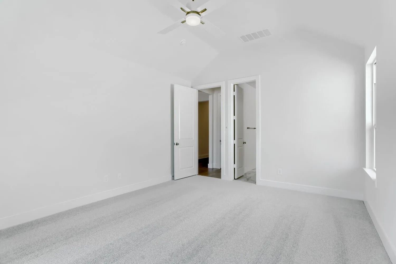 Vaulted ceiling with a ceiling fan, light-colored carpeting, white walls, and a window providing natural light