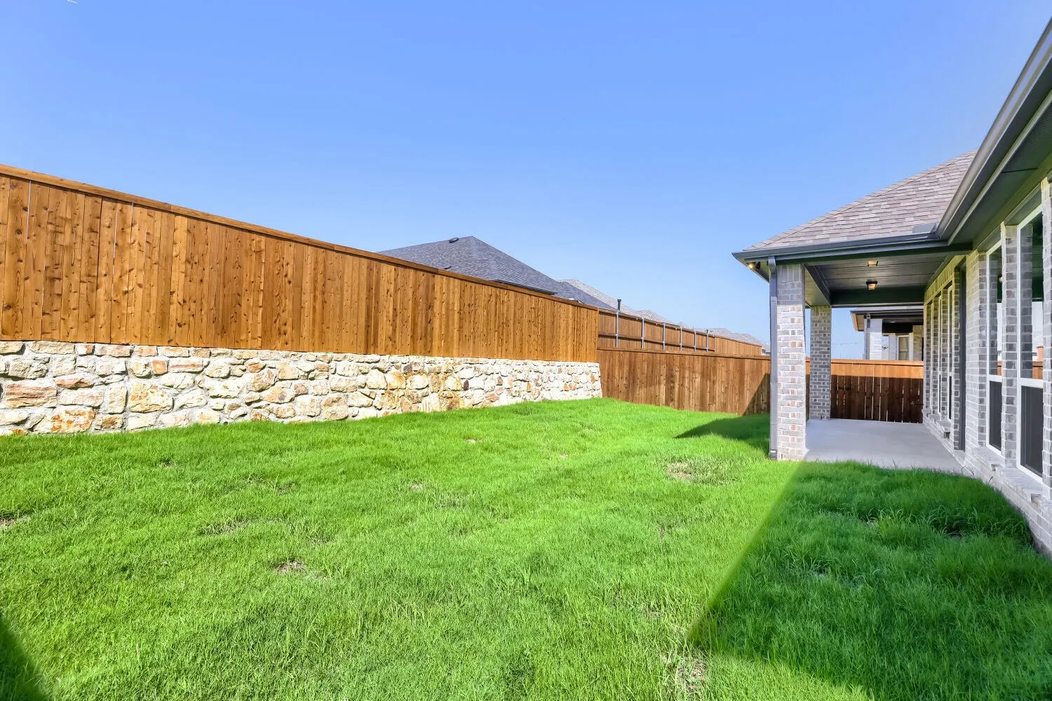 Expansive lawn area, wood privacy fencing with stone base, covered patio with brick columns, and multiple windows