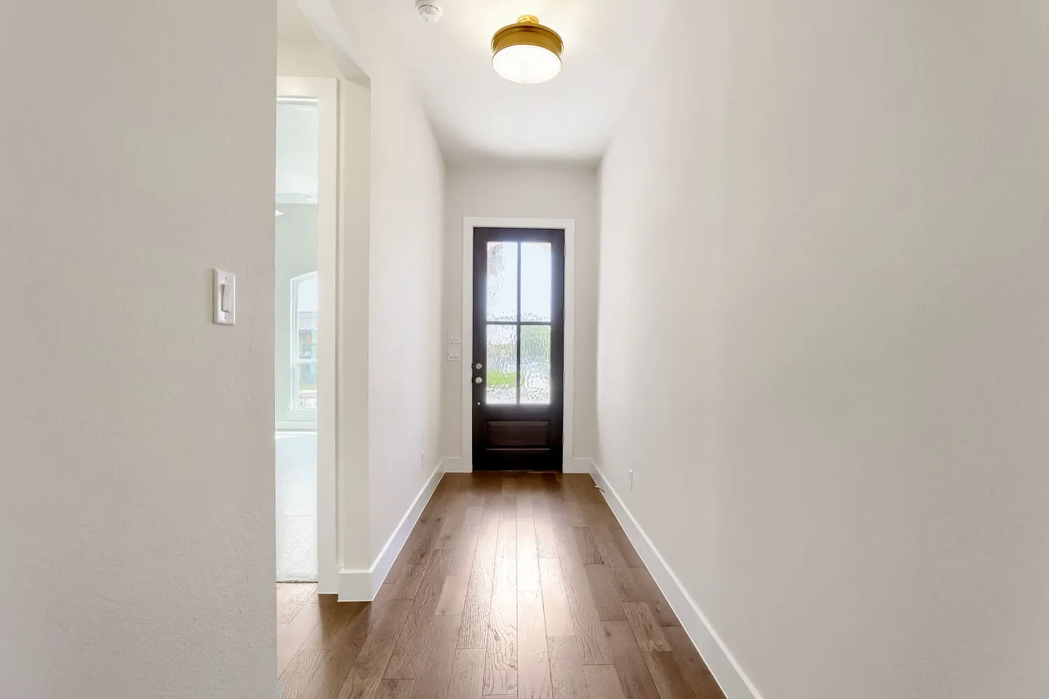 Wood-finish flooring with crisp white trim details, a dark paneled entry door with multiple lites, and a flush mount ceiling light fixture