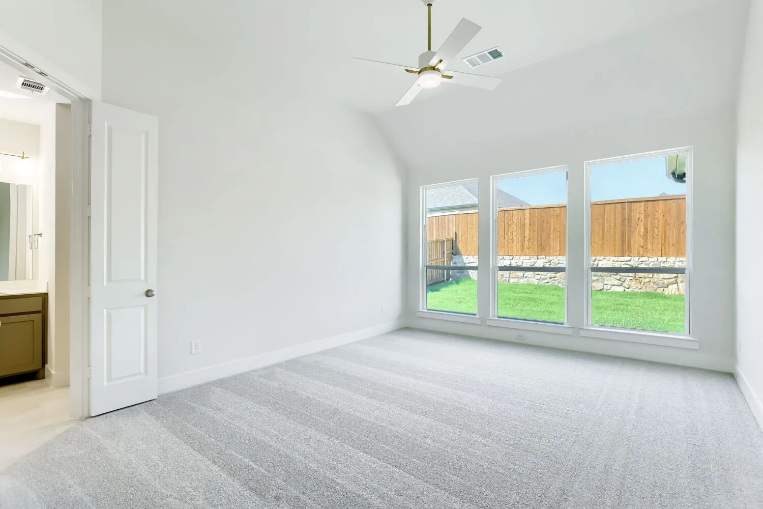 Vaulted ceiling with a ceiling fan, three large windows, light gray carpet, and white walls