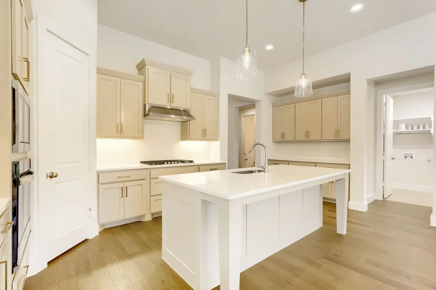 Kitchen featuring wood-finish flooring, recessed lighting, double ovens, and a center island with a sink and pendant lighting