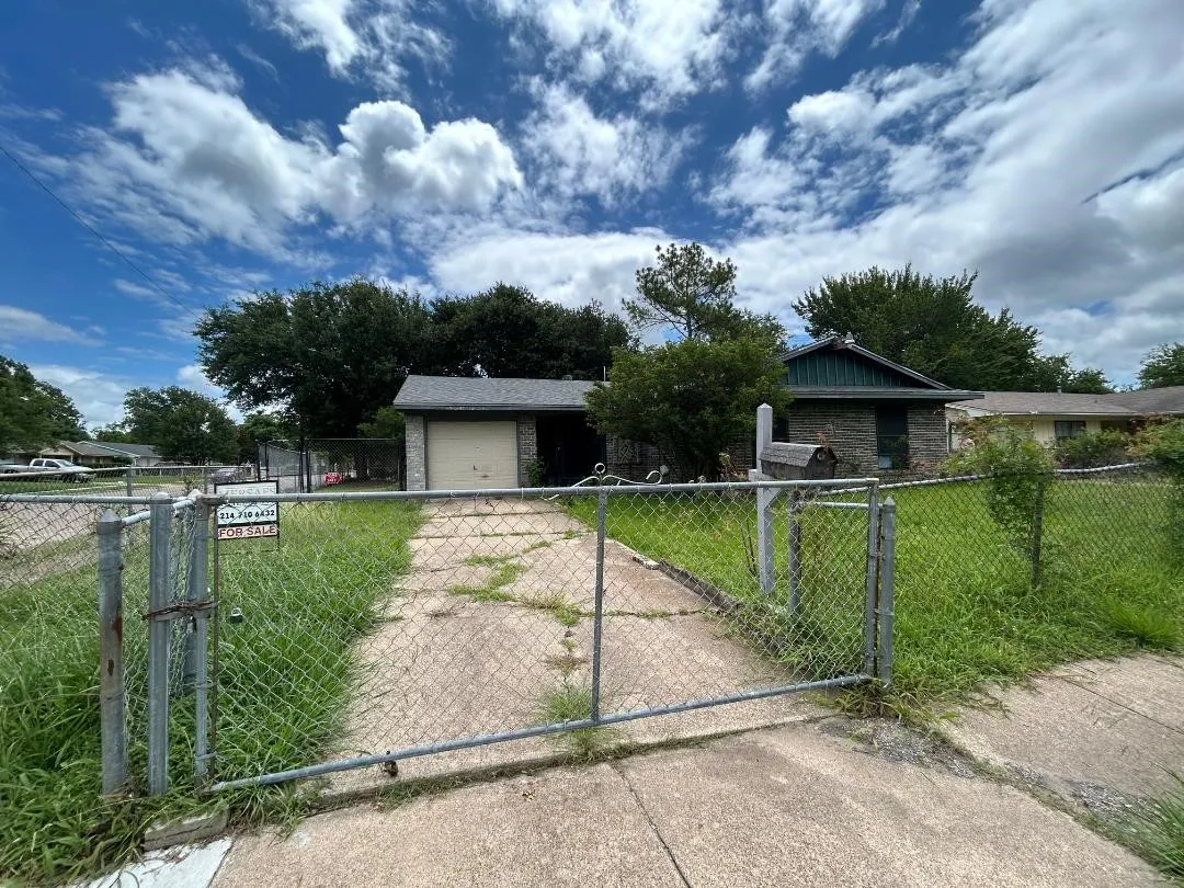 Single-story residential structure featuring a stone facade and an attached garage with a chain link fence in the front yard for extra security