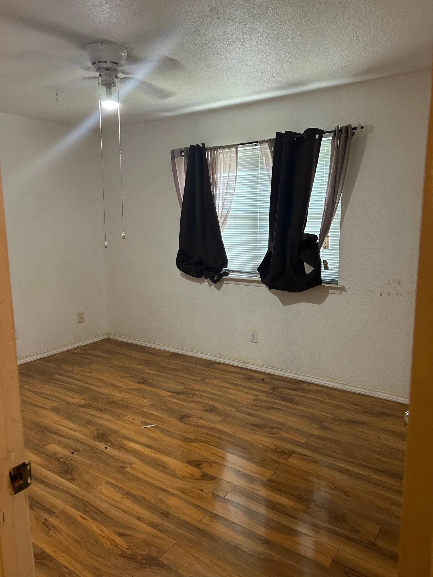Room featuring wood-finish flooring, a ceiling fan with integrated lighting, and a single window with horizontal blinds