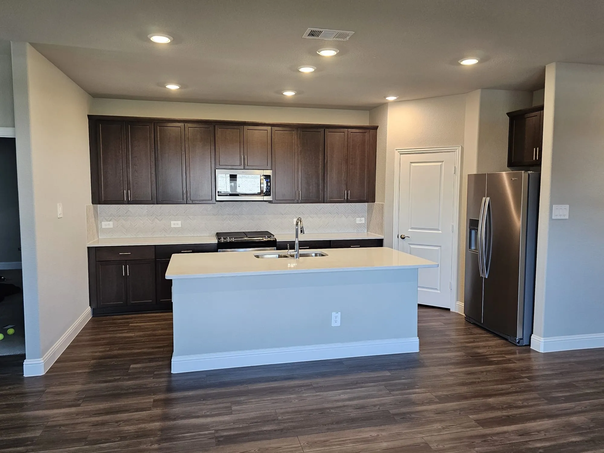 Kitchen featuring stainless steel appliances, dark hardwood / wood-style flooring, and a kitchen island with sink