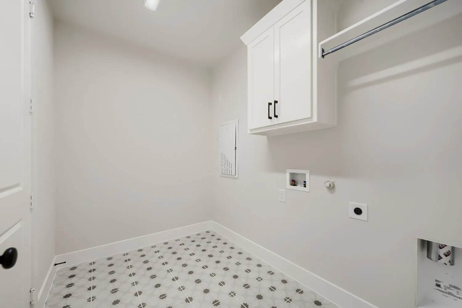 Laundry area featuring patterned floor tiles, white shaker-style cabinetry with matte black hardware, and a hanging rod
