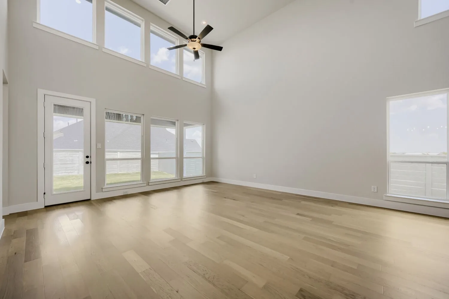 Spacious open living area showcasing wide-plank wood-finish flooring, soaring vaulted ceilings with clerestory windows, and French doors opening to outdoor space