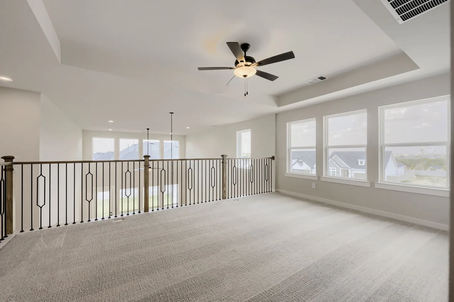 Spacious loft-style room featuring soaring ceilings with recessed lighting and ceiling fan, abundant natural light from multiple large windows, polished concrete flooring, and a striking metal railing that defines the open layout
