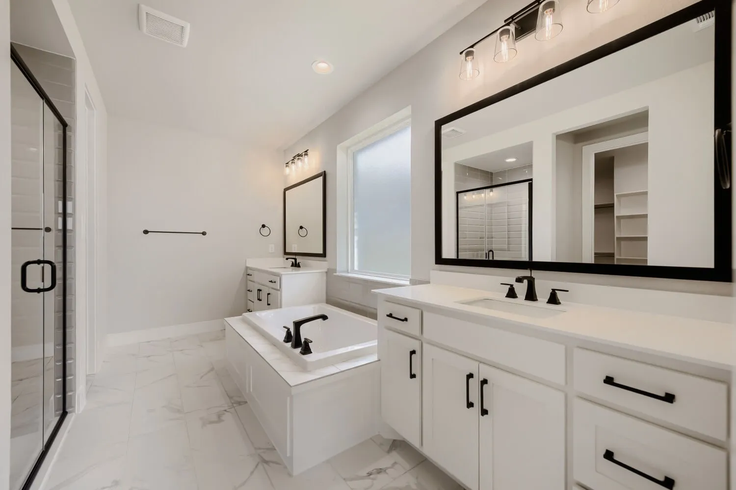 Dual vanity with white cabinetry, built-in bathtub, glass-enclosed shower, and large format tile flooring