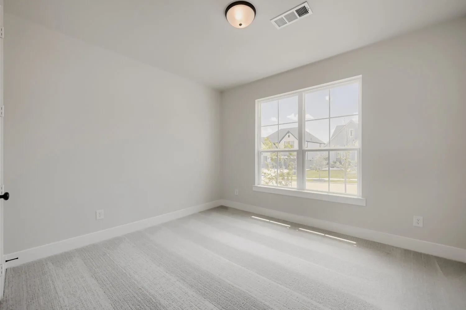 Light gray wall paint, large window, white trim, overhead flush-mount lighting, and light-toned carpet flooring