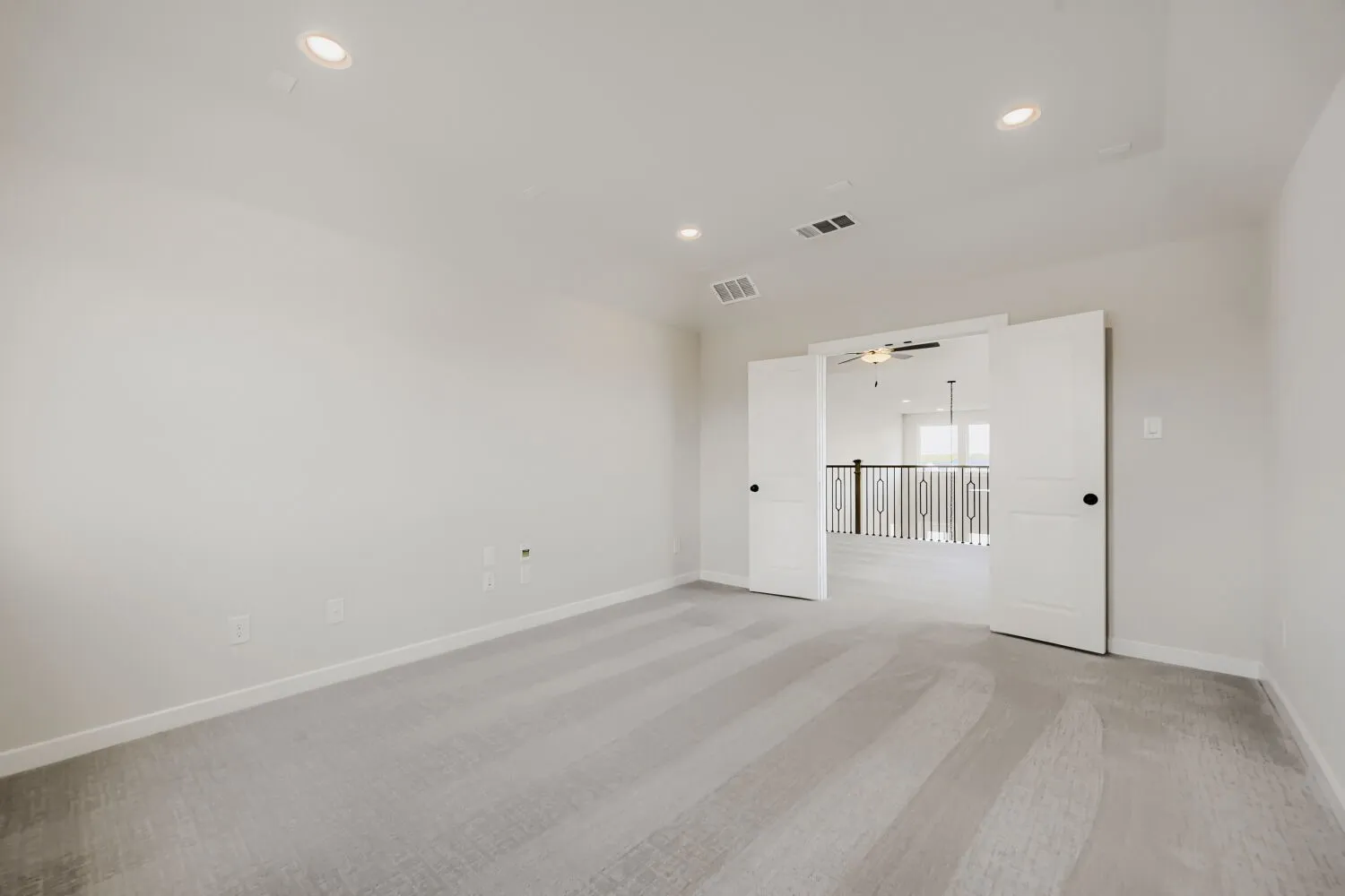 Spacious bedroom featuring wide-plank wood-finish flooring, recessed ceiling lighting, and dual glass sliding doors opening to an adjoining room with stair access