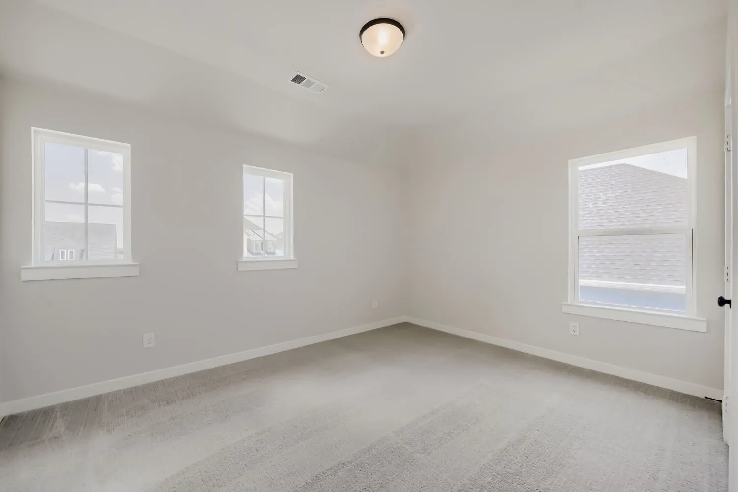 Neutral tone wall paint, carpeted flooring, three windows with white trim, and a ceiling-mounted light fixture