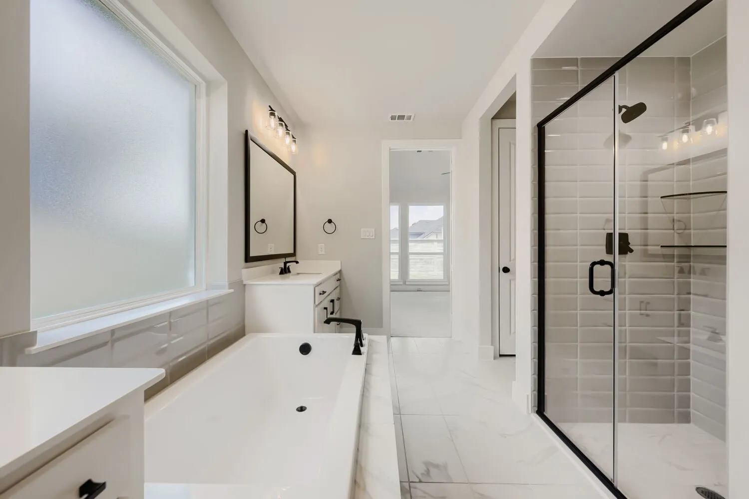 Freestanding bathtub with matte black fixtures, a frosted window, and a separate glass-enclosed shower featuring subway tile and built-in shelving