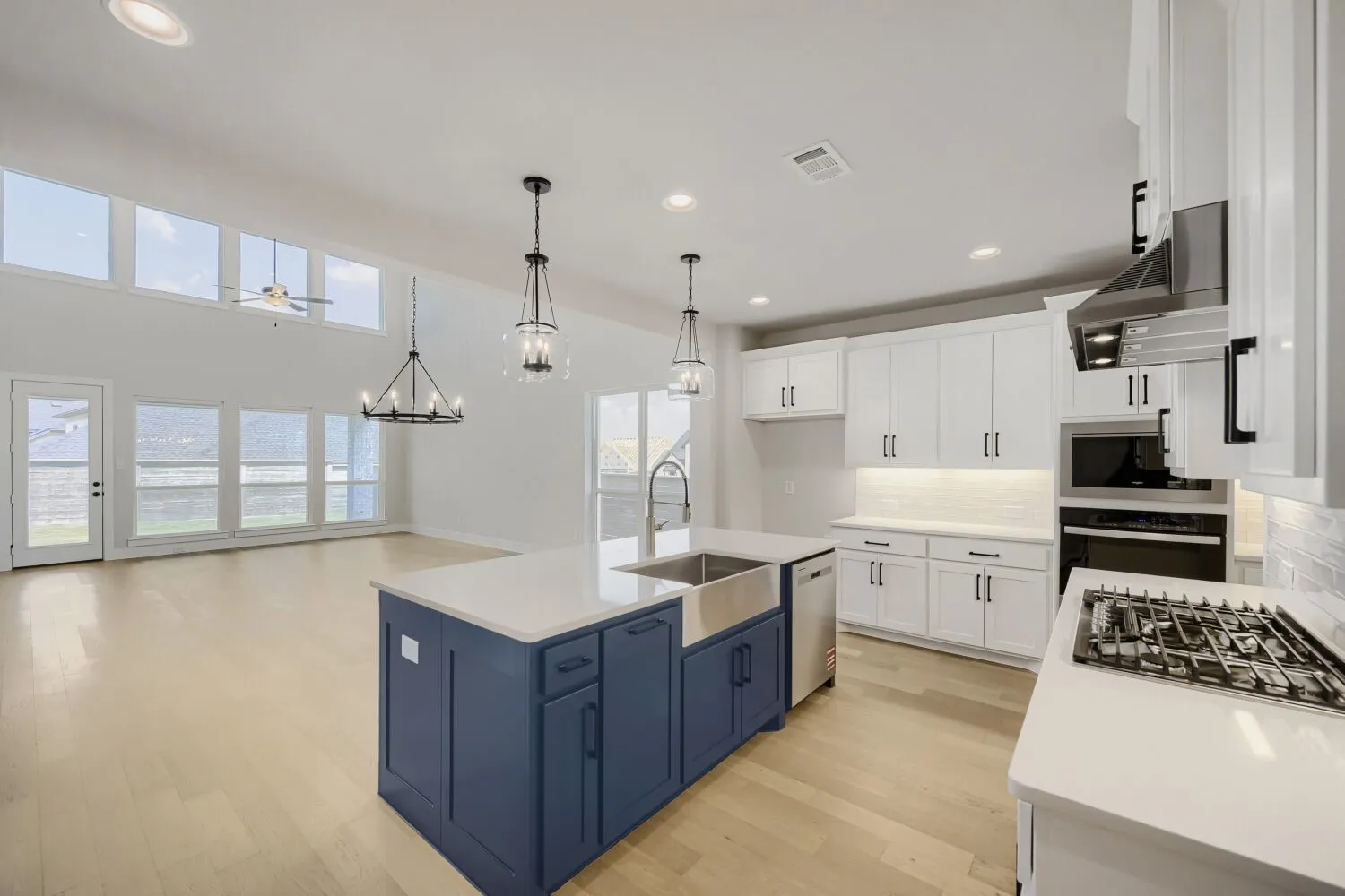 Gourmet kitchen featuring a navy blue center island with quartz countertops, stainless steel appliances including a gas cooktop and built-in oven, white cabinetry with brushed nickel hardware, and pendant lighting