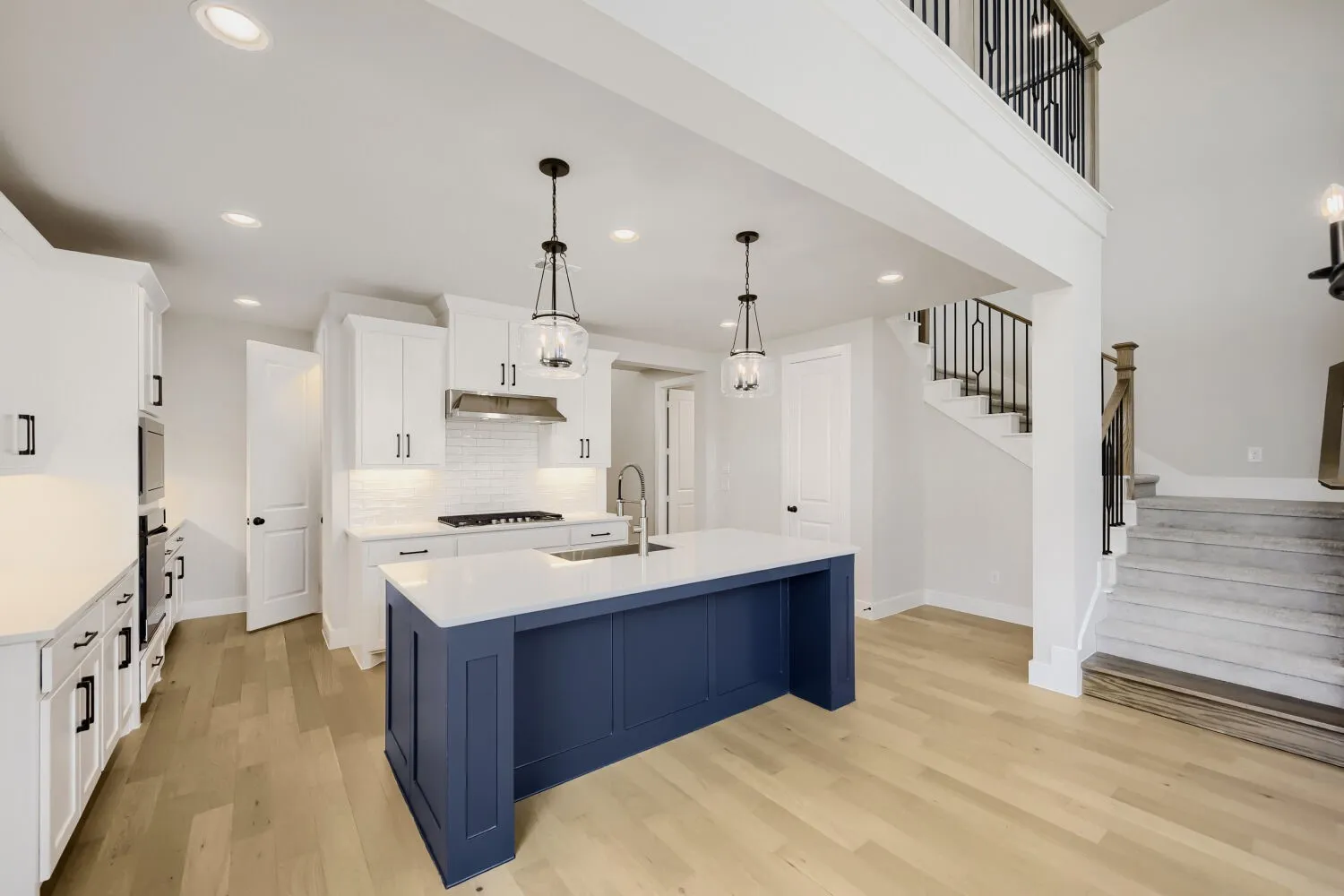 Open-concept kitchen and dining area featuring a custom navy blue island with white quartz countertop, stainless steel appliances including a gas cooktop, white cabinetry, pendant lighting, and wide-plank wood-finish flooring throughout