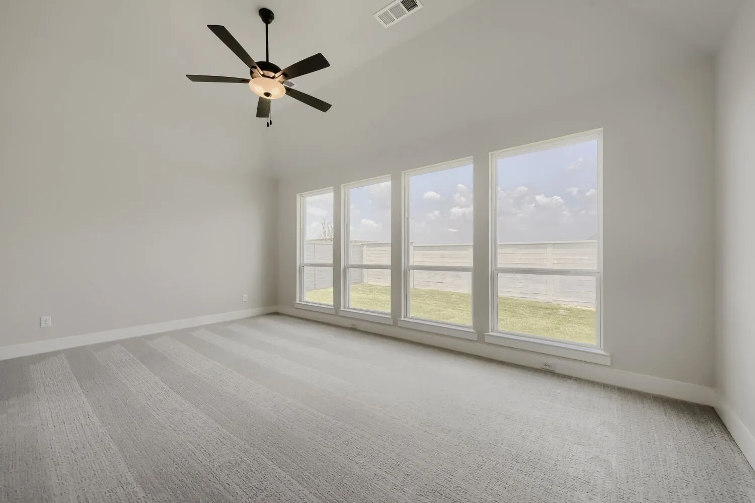 Vaulted ceiling, ceiling fan with integrated lighting, four large windows, neutral carpet flooring, and white painted walls