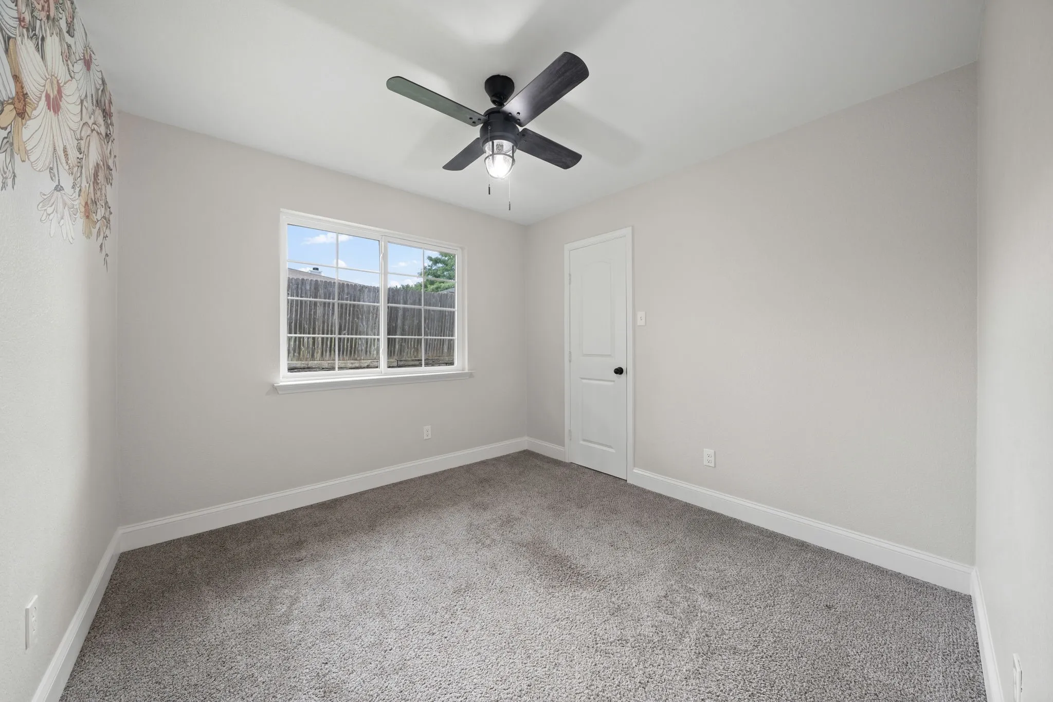 Carpeted interior room featuring a multi-pane window, white trim, a solid white door with black hardware, and a ceiling fan with integrated lighting