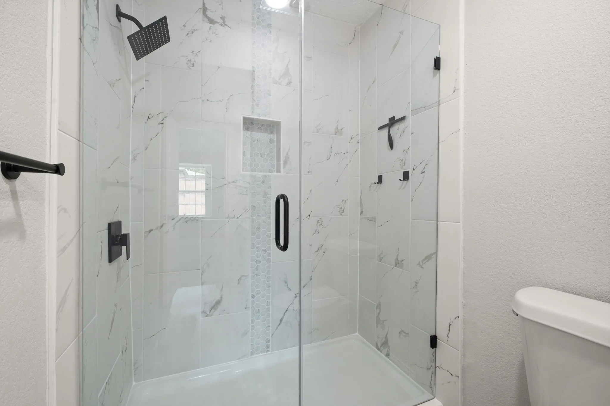 Glass-enclosed shower featuring white marble-look tile, a decorative tile accent strip, and matte black fixtures including a rain showerhead