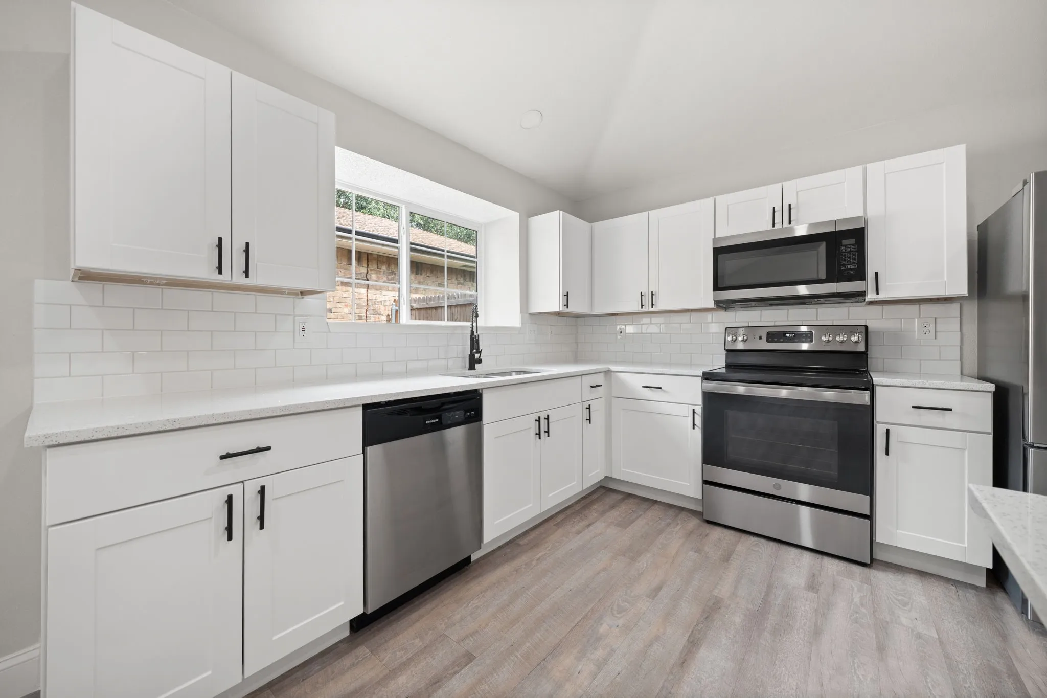 Kitchen featuring white shaker-style cabinetry, stainless steel appliances, a white subway tile backsplash, and light-toned wood-finish flooring