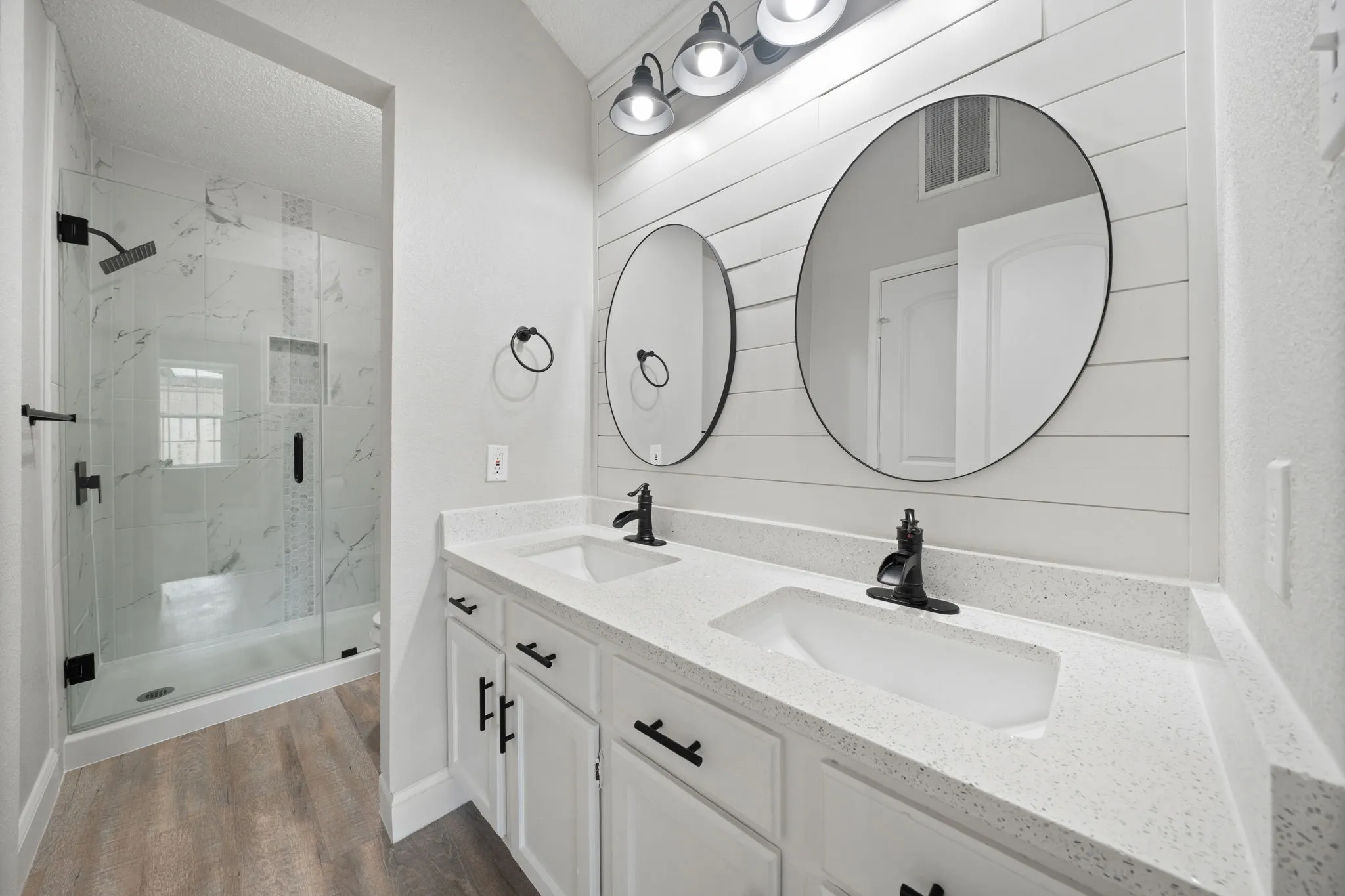 Bathroom featuring a dual vanity with white cabinetry, light-toned countertops, and two circular mirrors