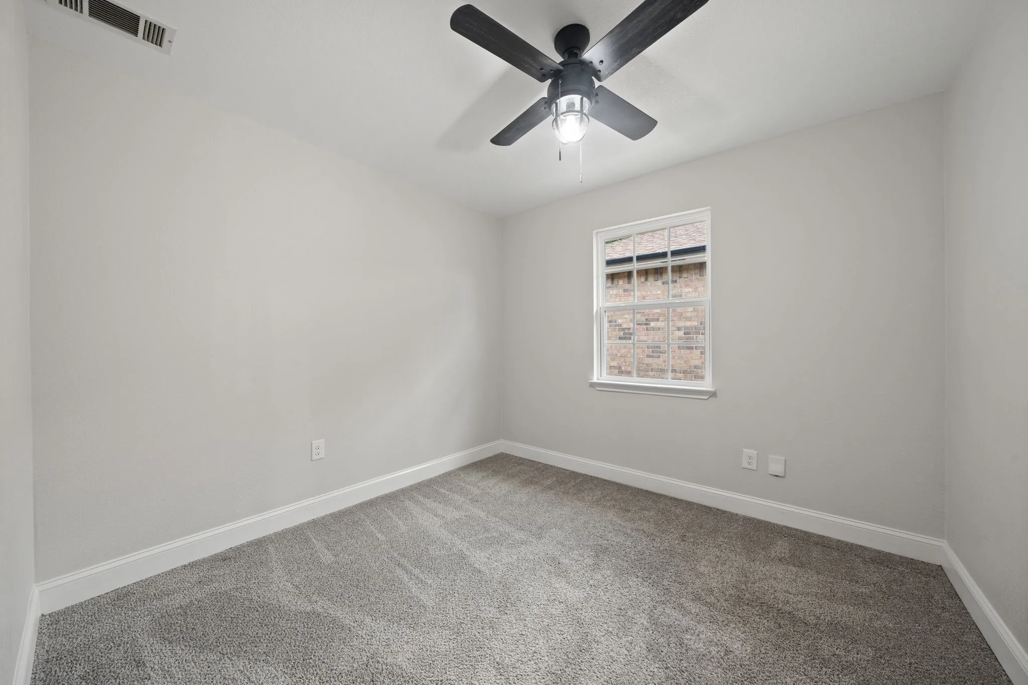 Neutral-toned room featuring a single window, grey carpet flooring, white baseboards, and a black ceiling fan with integrated lighting