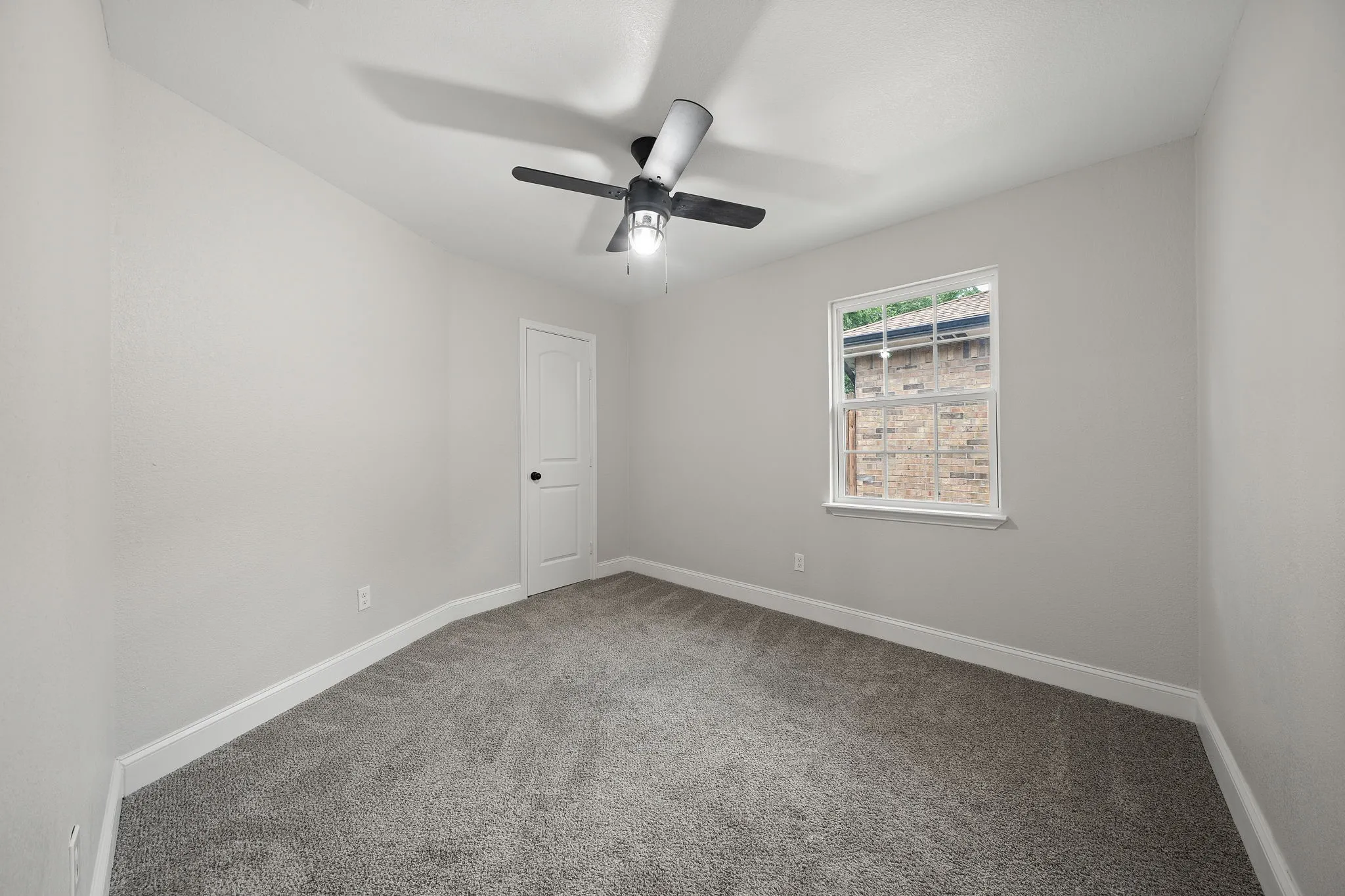 Carpeted room with a ceiling fan, a window with white trim, a white paneled door, and neutral-toned walls