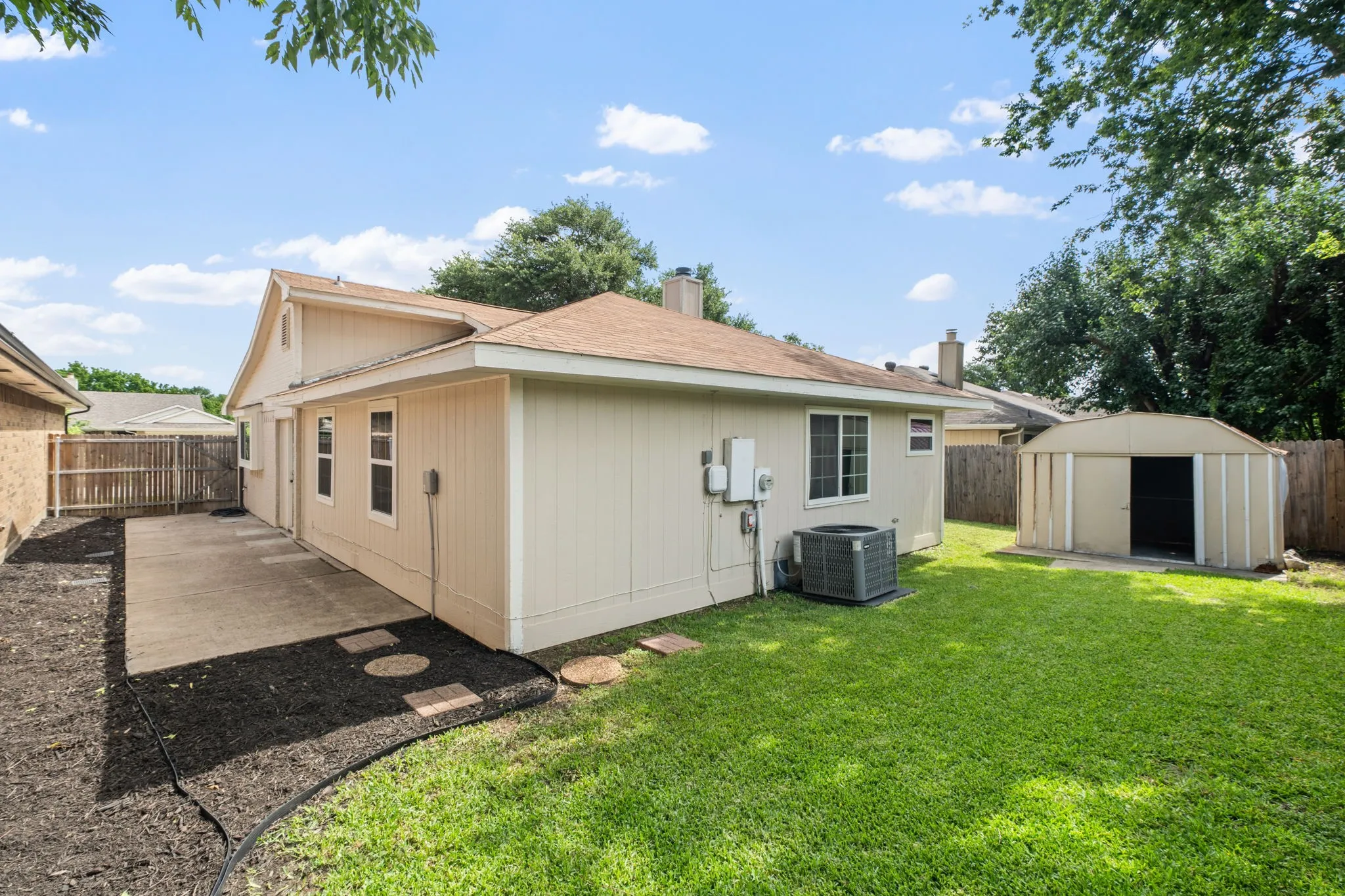 Expansive backyard featuring a concrete patio, stepping stones, and a large storage shed