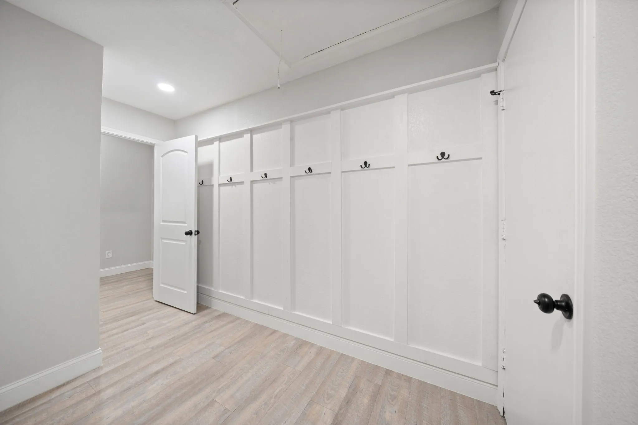 Built-in board and batten wall with integrated hooks, light wood-finish flooring, recessed lighting, and white trim