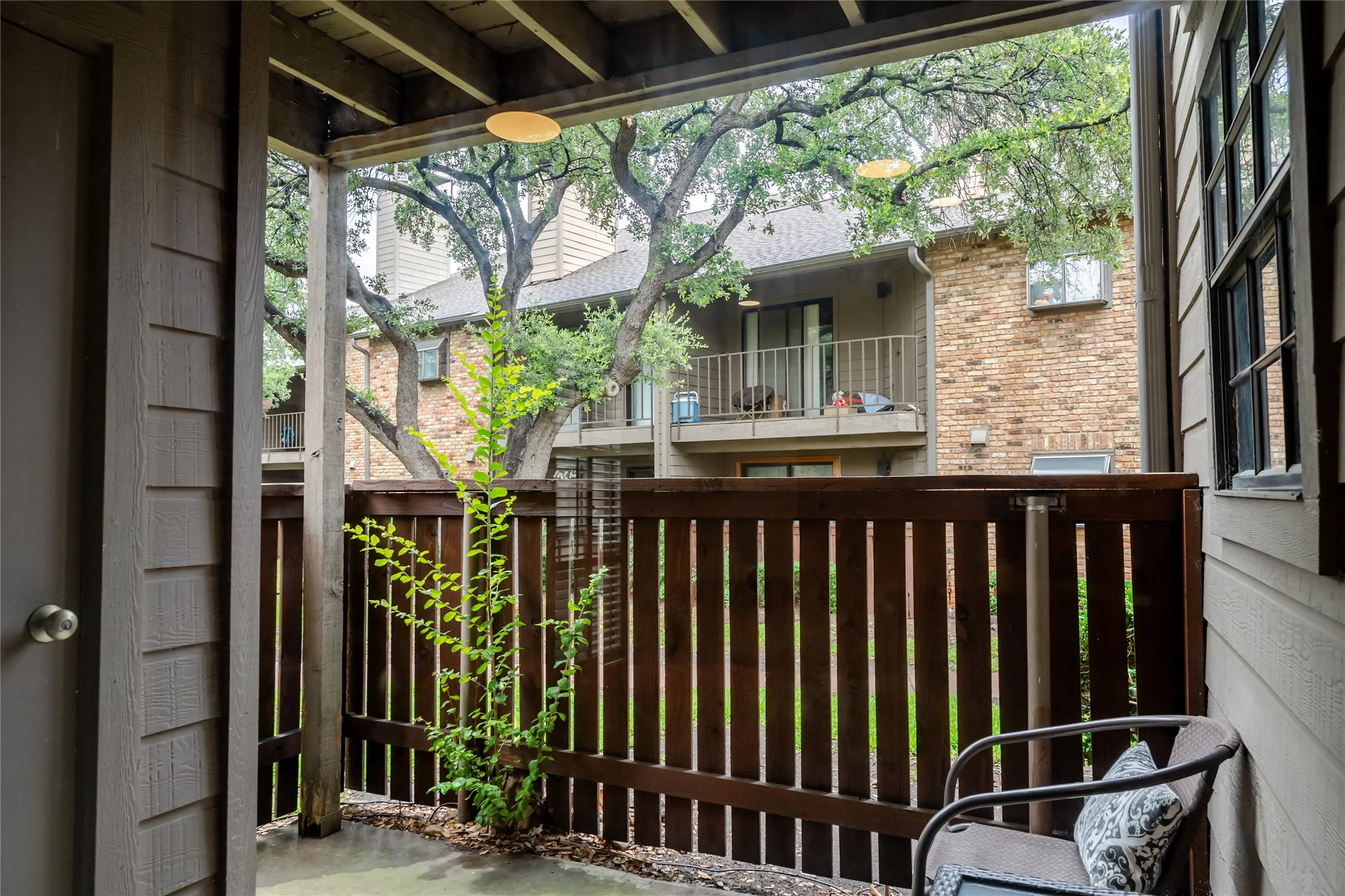 Covered patio featuring a slatted wood privacy fence, concrete flooring, and a ceiling-mounted light fixture