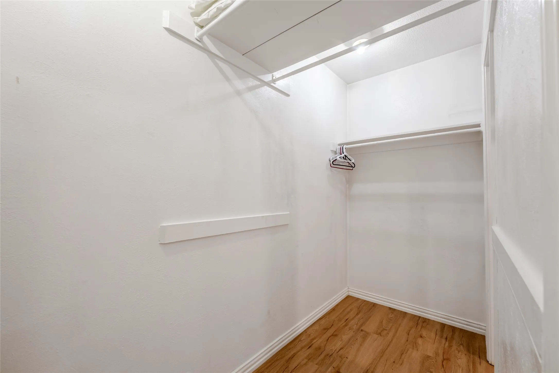 Walk-in closet featuring wood-finish flooring, white baseboards, and built-in shelving with a hanging rod