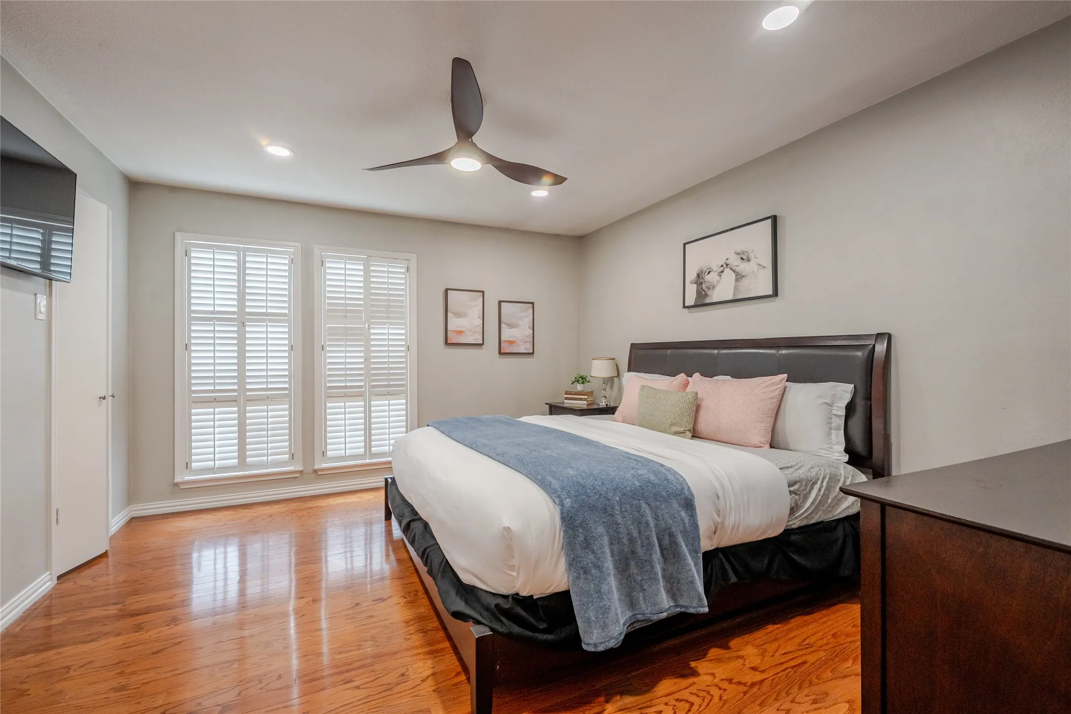 Spacious room featuring wood-finish flooring, two large windows with plantation shutters, recessed lighting, and a contemporary ceiling fan