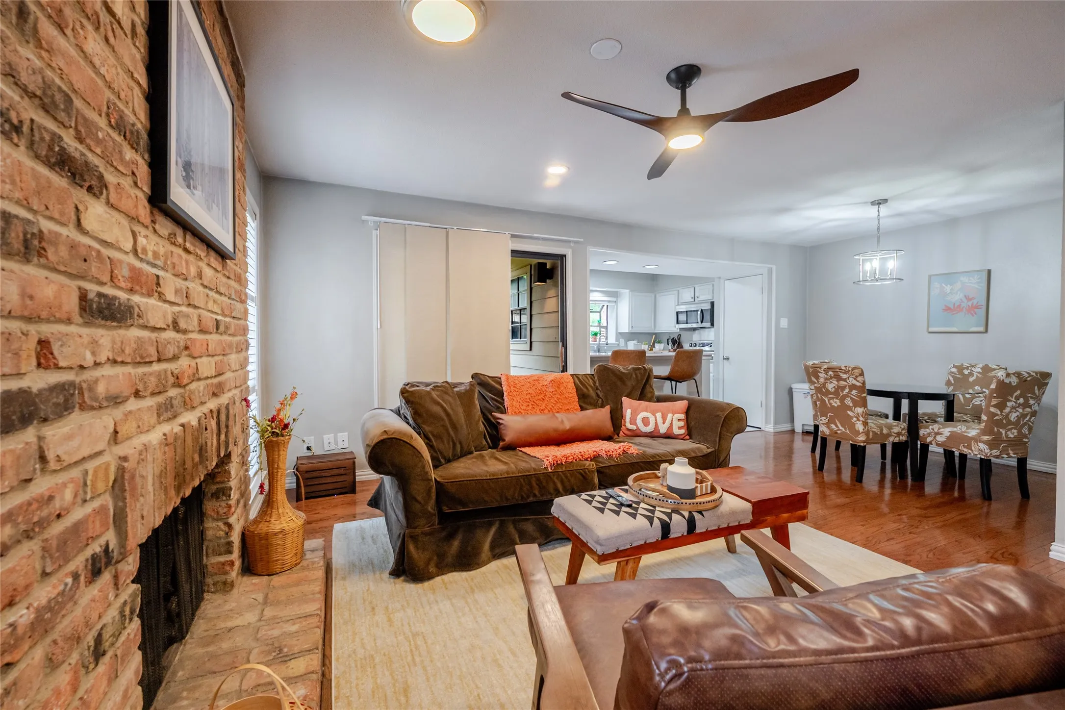 Spacious living area featuring a brick fireplace, wood-finish flooring, and a contemporary ceiling fan