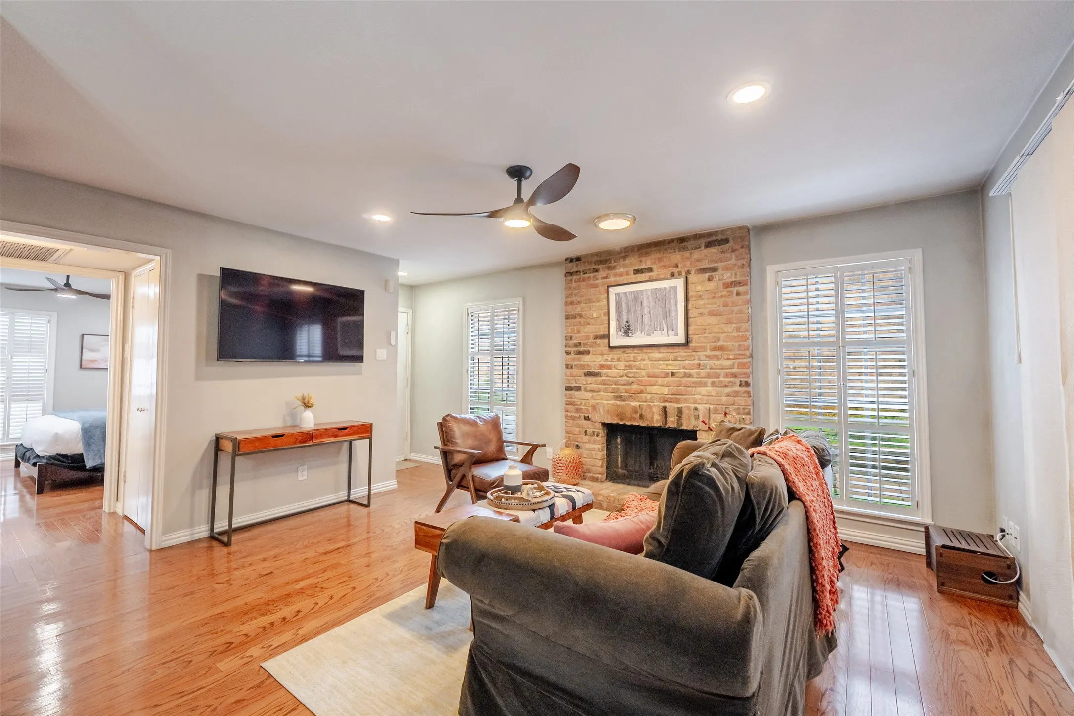 Living area featuring polished wood-finish flooring, a brick fireplace with a dark firebox, and recessed lighting