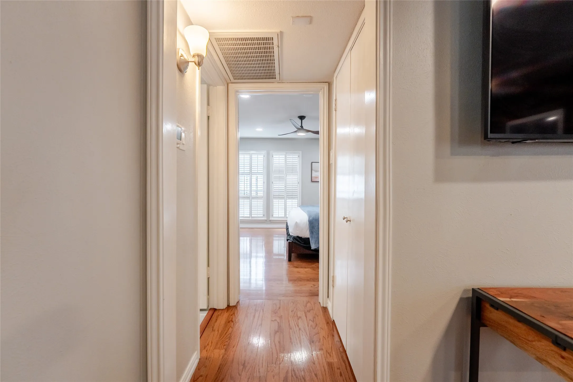 Hallway featuring wood-finish flooring, white walls, and a wall-mounted sconce