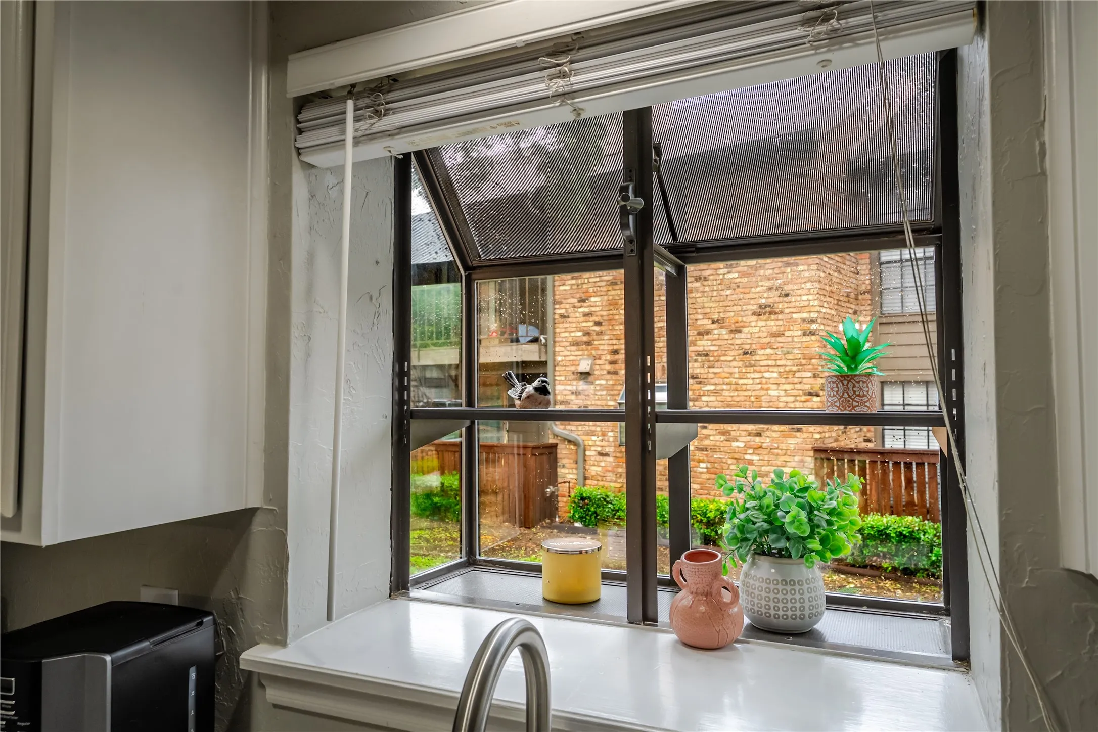 Kitchen window featuring a stainless steel faucet, a white countertop, and white cabinetry