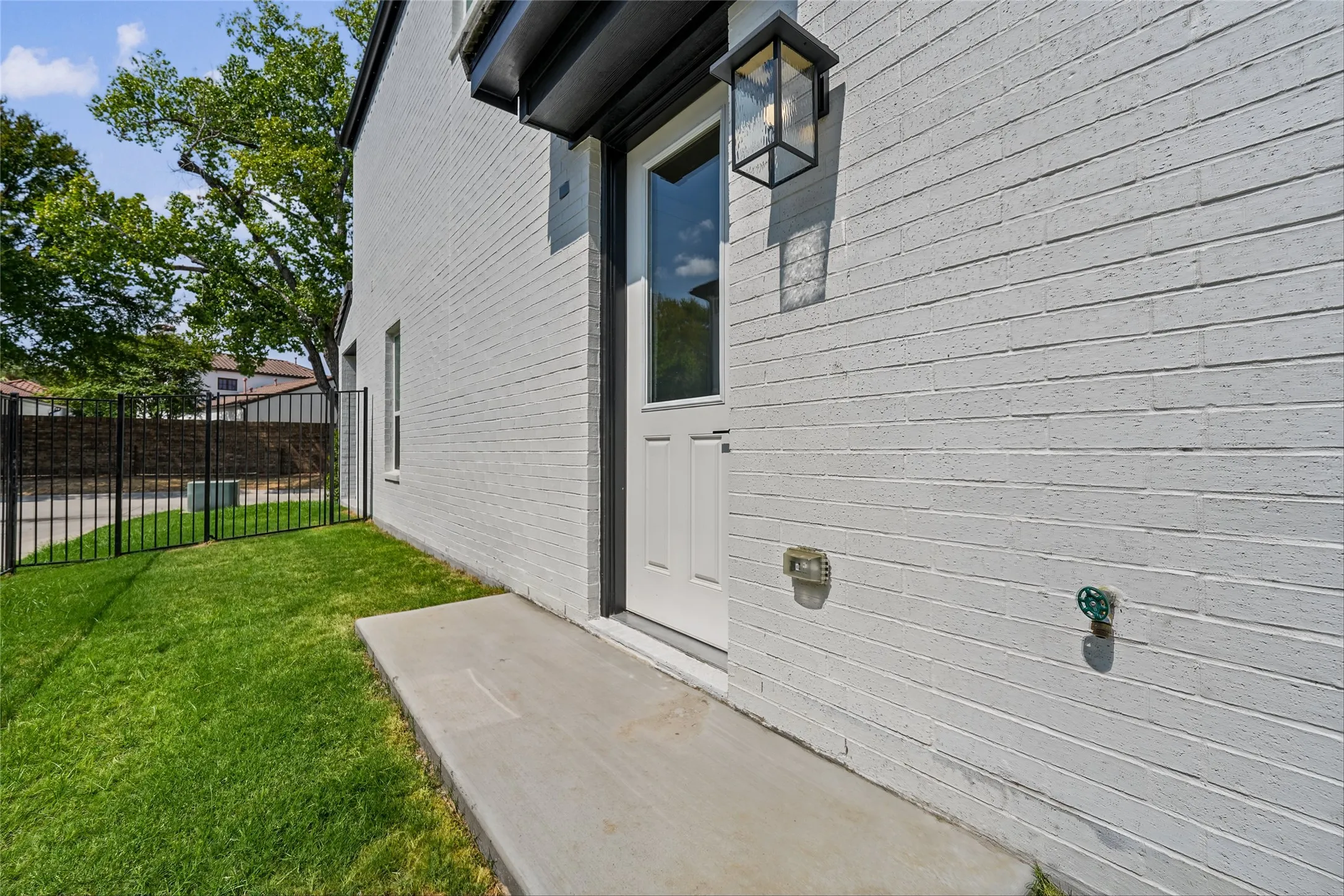 White painted brick exterior, single paneled door with glass insert, black exterior lighting fixture, concrete walkway, and a manicured lawn