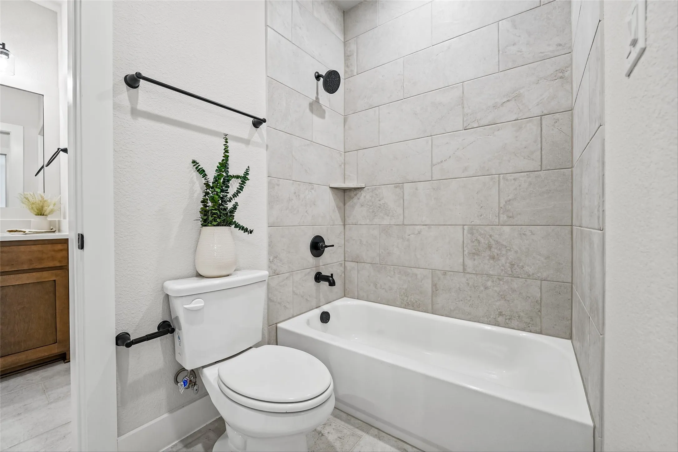 Tub/shower combination with light-toned tiled surround, matte black fixtures, and a recessed soap dish