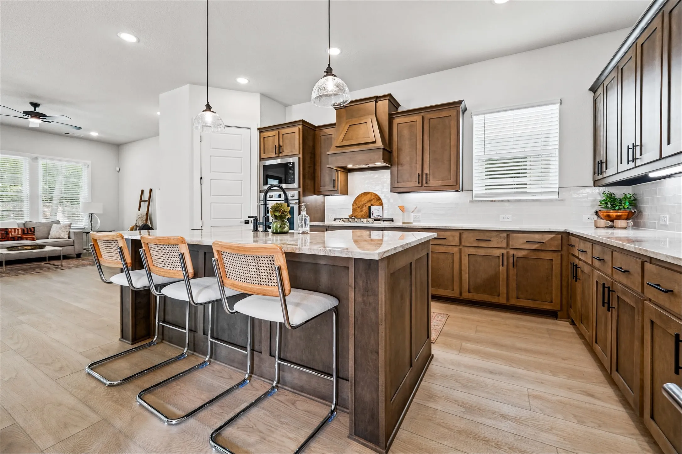 Kitchen featuring wood-finish flooring, a large central island with pendant lighting, rich wood cabinetry, stainless steel appliances, and a tile backsplash