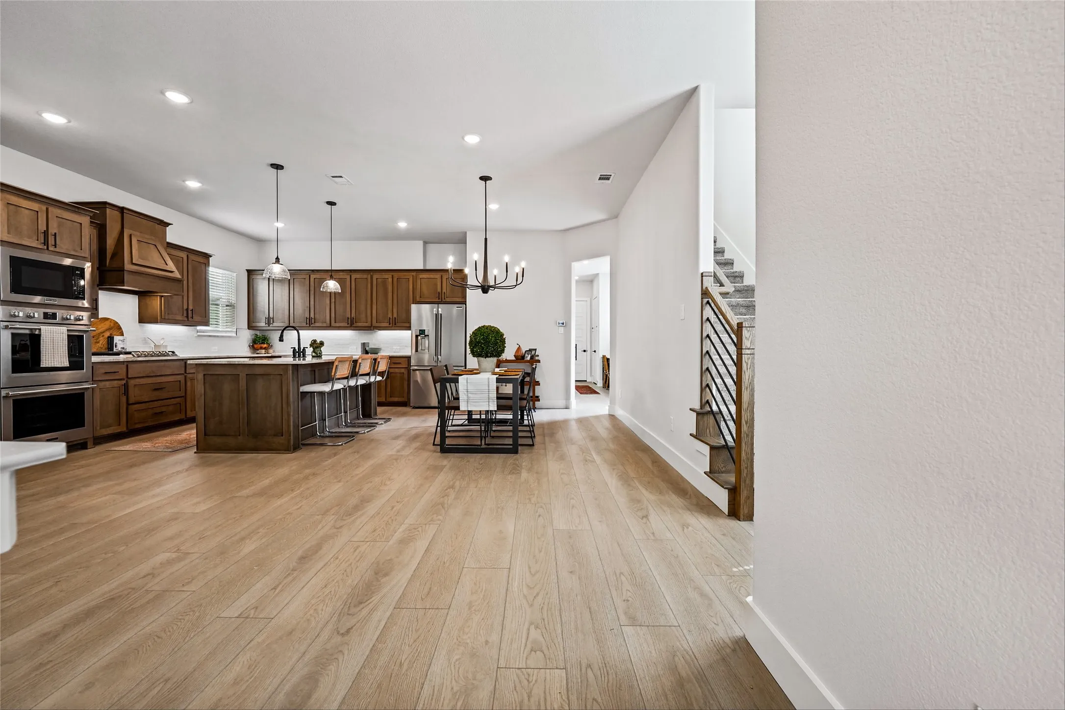 Expansive wood-finish flooring throughout, kitchen featuring stainless steel appliances, a large island with seating, dark wood cabinetry, and recessed lighting