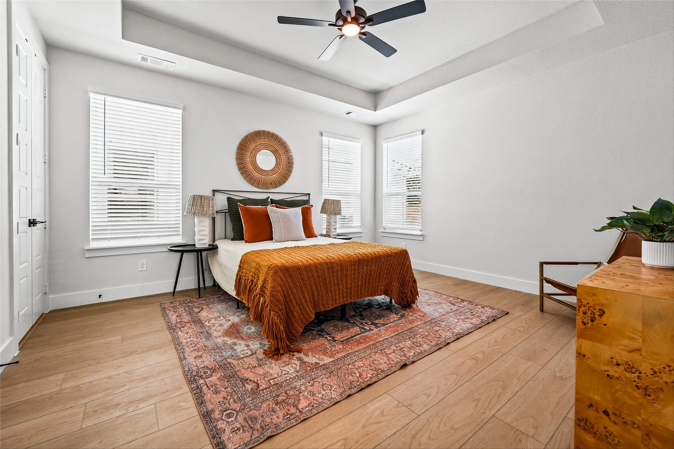 Tray ceiling with a ceiling fan, wood-finish flooring, and multiple windows with blinds