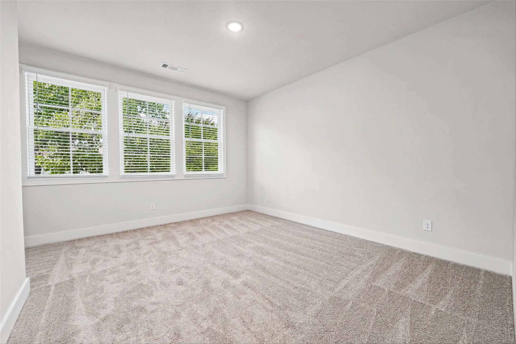 Neutral wall paint, three windows with blinds, recessed ceiling light, and carpet flooring