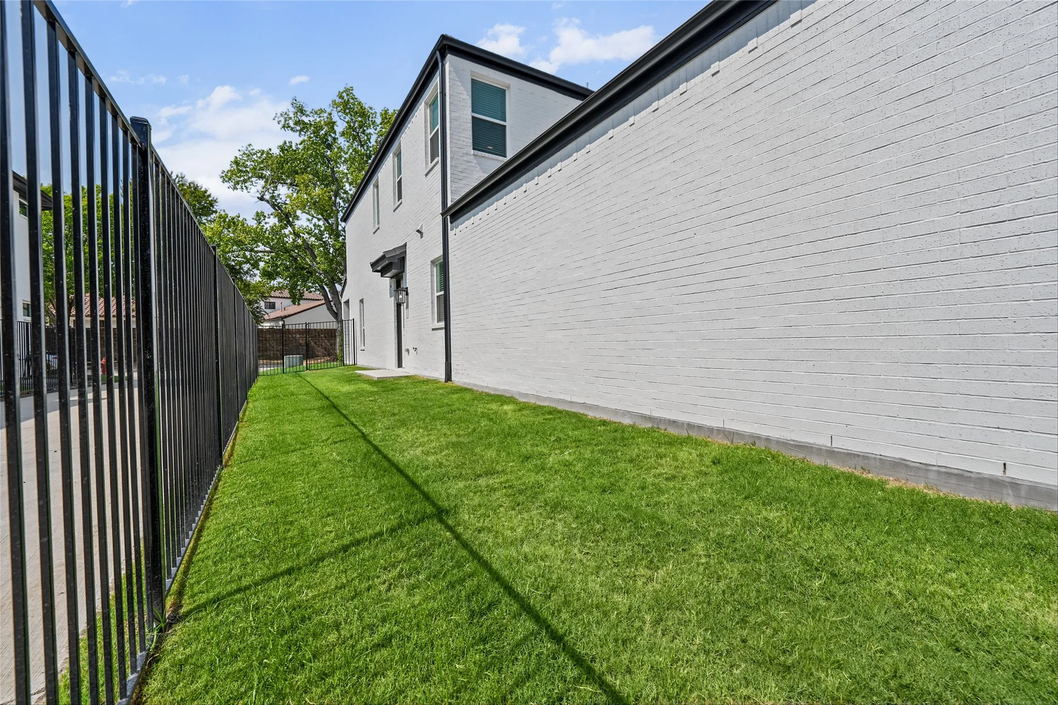 Manicured lawn area with a black metal fence, painted brick exterior, and dark trim details
