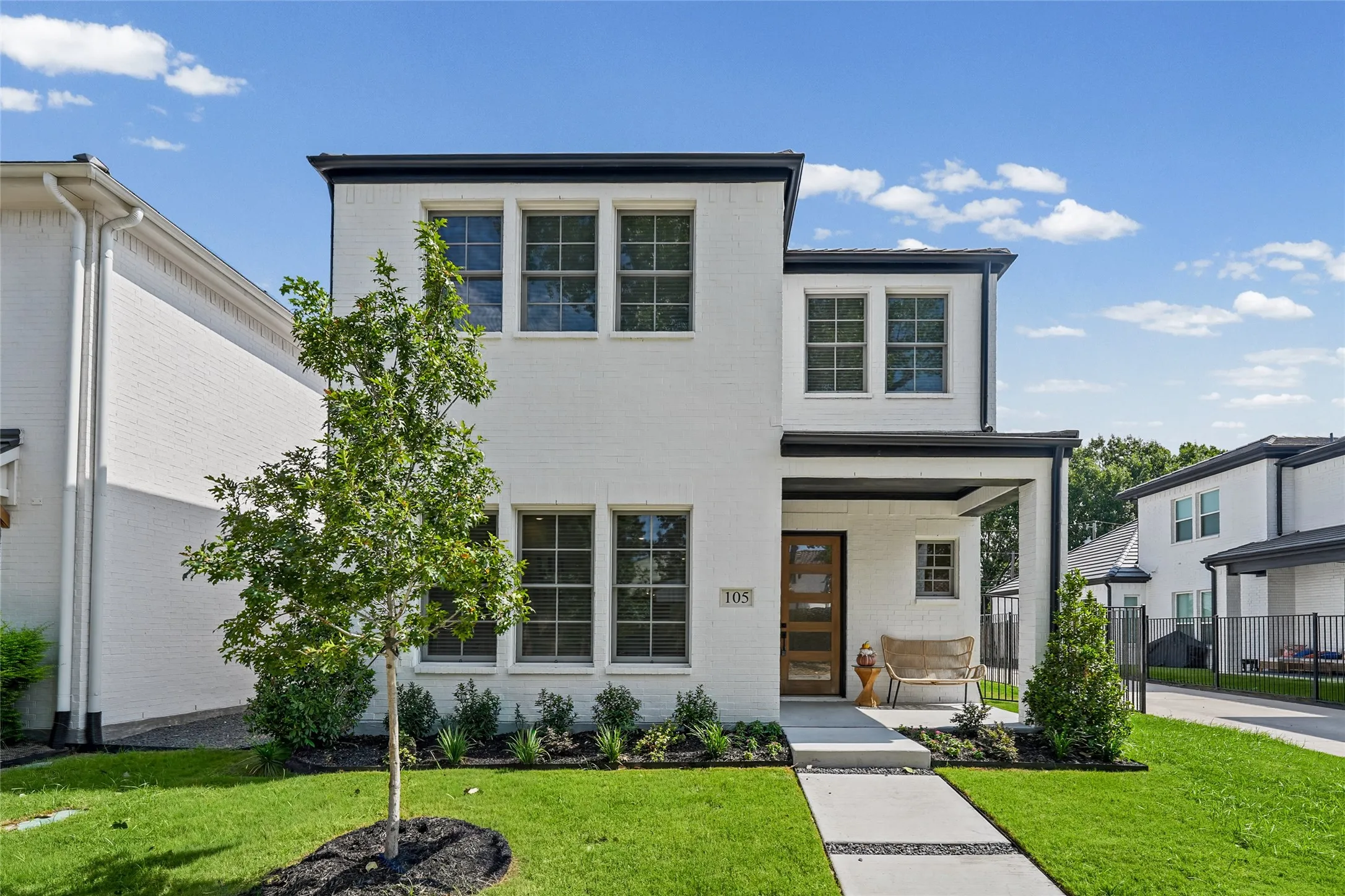 Contemporary white brick exterior with black trim, covered porch, wood-paneled entry door, and concrete walkway