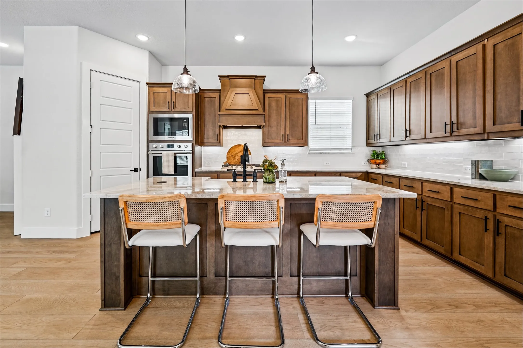 Expansive kitchen island with seating, wood-finish flooring, recessed lighting, and built-in stainless steel appliances